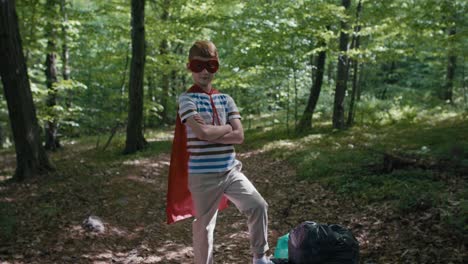 Ginger-caucasian-boy-wearing-superhero-costume-standing-with-garbage-bags.